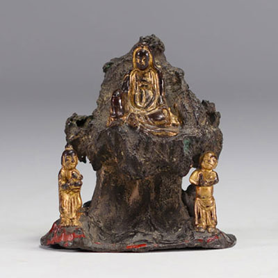 Bronze Guanine sculpture seated on a rock and surrounded by two figures.