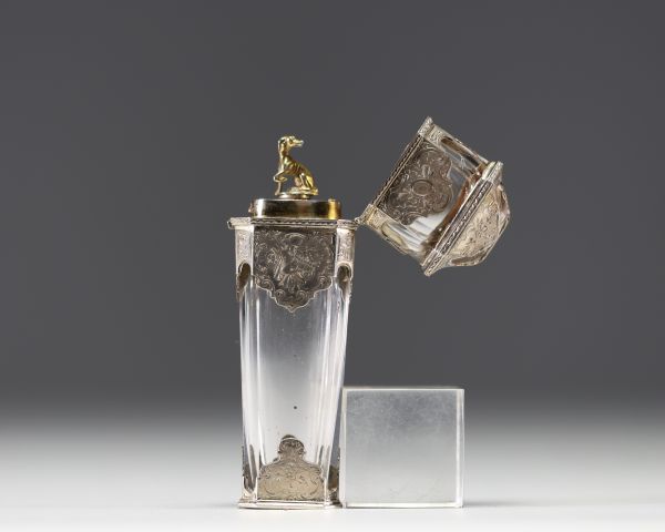 A rare solid silver and crystal perfume bottle decorated with musical instruments, foliage and flowers, the stopper representing a greyhound in vermeil, 19th century.