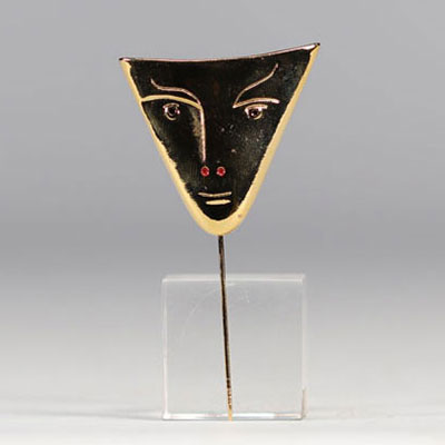 Jean Cocteau.  « Face triangle ».  Bronze poli et doré à l'or fin, émail  rouge. Yeux : saphirs.  Signé « Jean Cocteau » au dos.  Numéroté 171/200.  Dessin de 1958.  Dimensions : 4 x 4,5 x 6,7 cm.