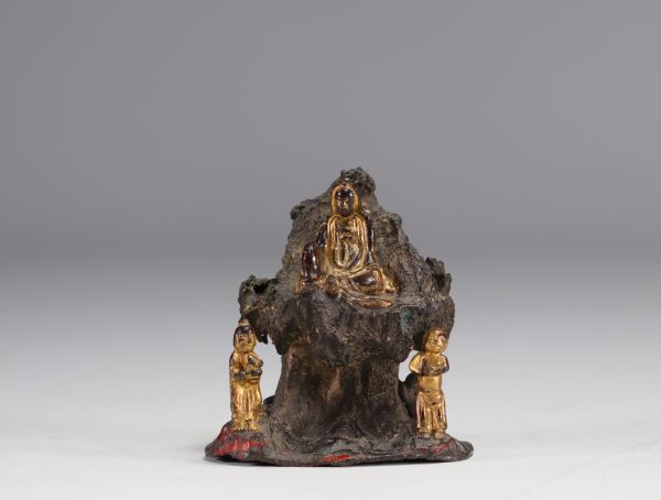 Bronze Guanine sculpture seated on a rock and surrounded by two figures.