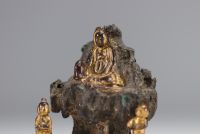 Bronze Guanine sculpture seated on a rock and surrounded by two figures.