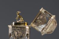 A rare solid silver and crystal perfume bottle decorated with musical instruments, foliage and flowers, the stopper representing a greyhound in vermeil, 19th century.