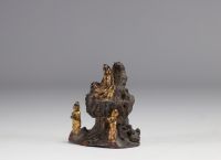 Bronze Guanine sculpture seated on a rock and surrounded by two figures.