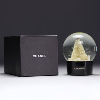 Boule à neige CHANEL représentant le flacon du parfum CHANEL n° 5, de sacs cadeaux CHANEL, d'un sapin et surmonté du logo CC